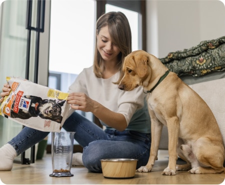 Moteris pila „Hill's Pet Nutrition“ maistą į matavimo indą, kol šuo atidžiai žiūri.