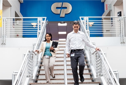 „Colgate-Palmolive“ darbuotojai leidžiasi laiptais, o už jų nugaros ant mėlynos sienos matomas „Colgate-Palmolive“ logotipas.