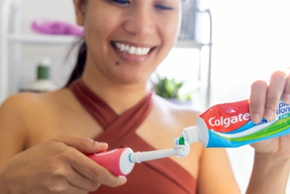 Moteris, šypsodamasi, vonios kambaryje tepa „Colgate“ dantų pastą ant dantų šepetėlio.